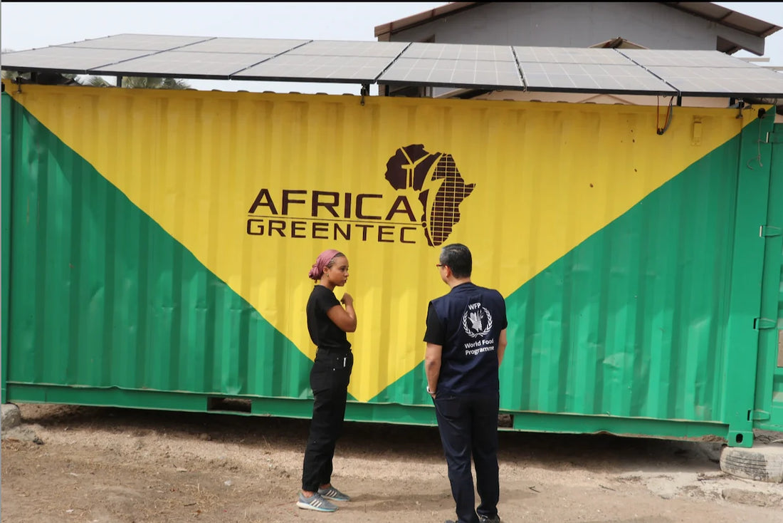 Zwei Personen stehen vor einem gelb-grünen Container mit der Aufschrift „Africa GreenTec“ und einer stilisierten Karte Afrikas. Auf dem Container sind Solarpanele montiert.