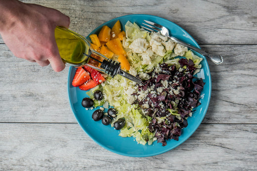 Ein farbenfroher Teller mit einer frischen Mischung aus Salat, Gemüse und Früchten, verfeinert mit Olivenöl. Die Szene hebt gesunde Ernährung und frische Zutaten hervor.